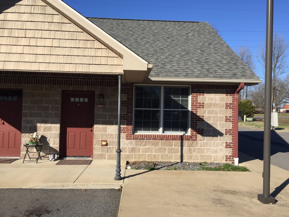 A small brick building with a red door and large window on a sunny day.