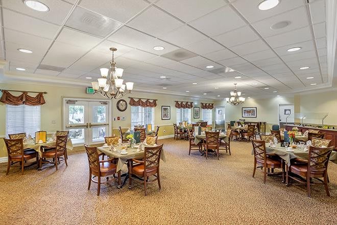 Spacious dining area with multiple tables and chairs, adorned with elegant chandeliers and large windows.