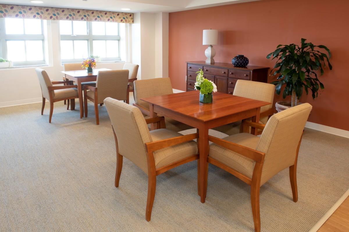 A cozy dining area featuring a wooden table with matching chairs and a centerpiece of flowers, set against a warm-toned wall.