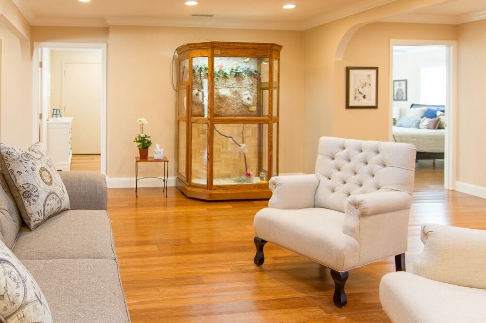 A cozy living room with a white armchair, wooden floors, and a display cabinet.