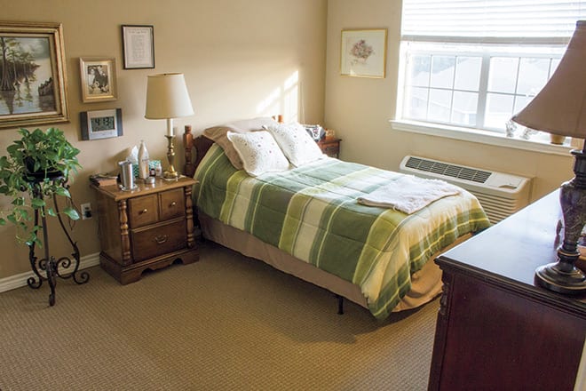 A cozy bedroom with a neatly made bed and a nightstand beside it, illuminated by natural light from the window.