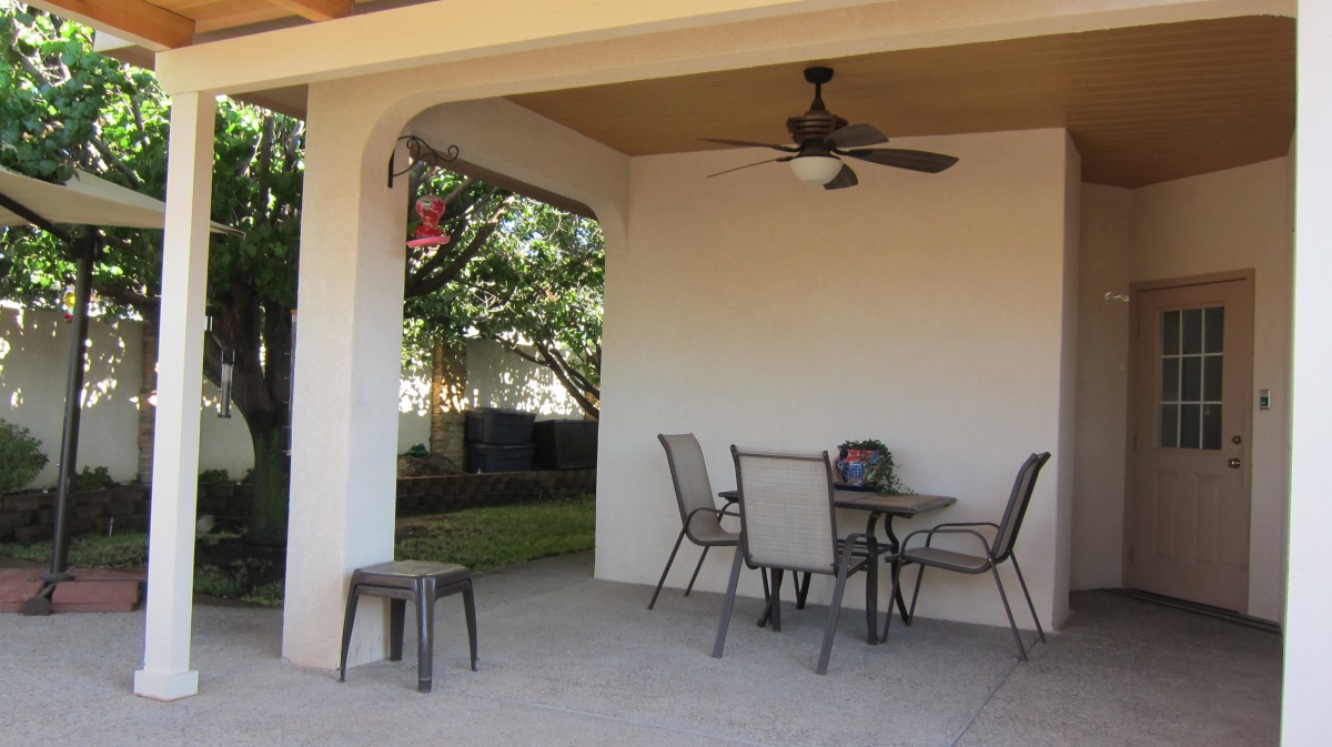 A cozy outdoor patio with a table, chairs, and a ceiling fan under a covered area.