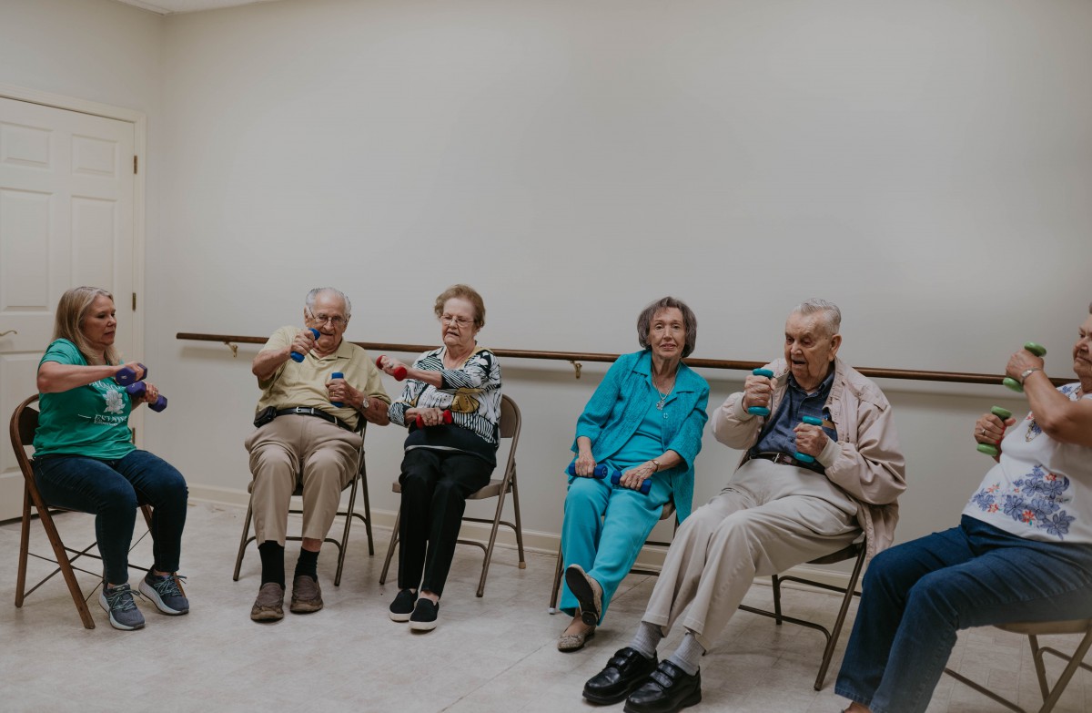 A group of seniors sitting in chairs, smiling and socializing indoors.