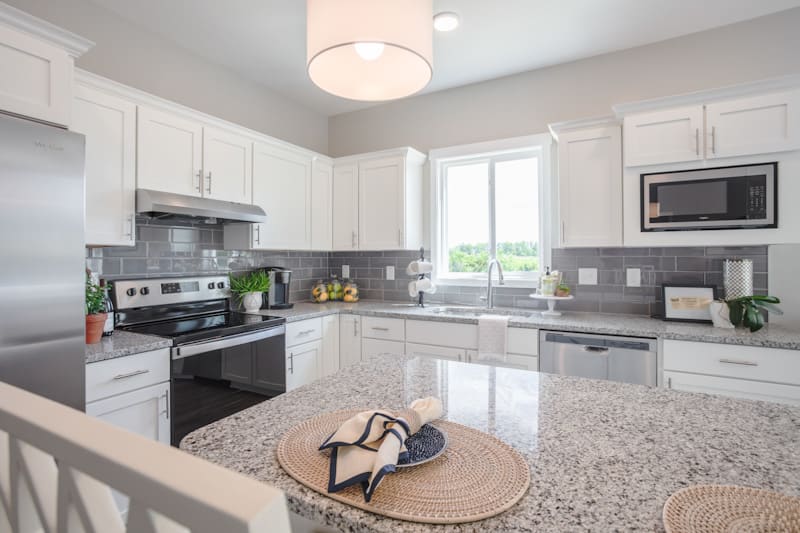 A modern kitchen with white cabinets, granite countertops, and stainless steel appliances.