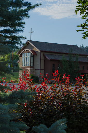 A serene view of a church surrounded by vibrant red flowers in a peaceful landscape.