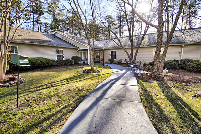 A house with a curved pathway in a sunlit yard surrounded by trees.