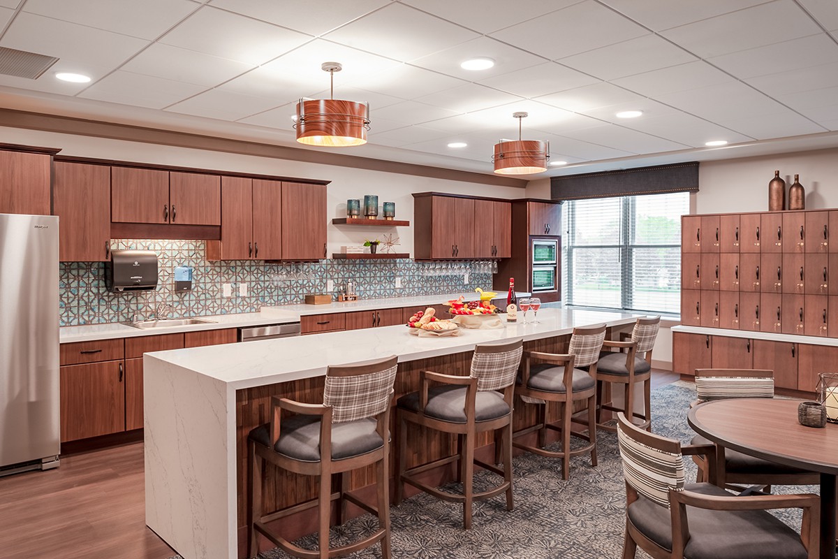 A modern kitchen with a large island and stylish bar stools, featuring wooden cabinets and contemporary lighting.