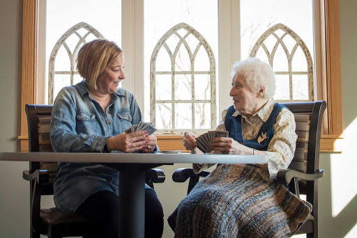 A caregiver enjoys a card game with an elderly woman, highlighting the joy of companionship and social interaction.