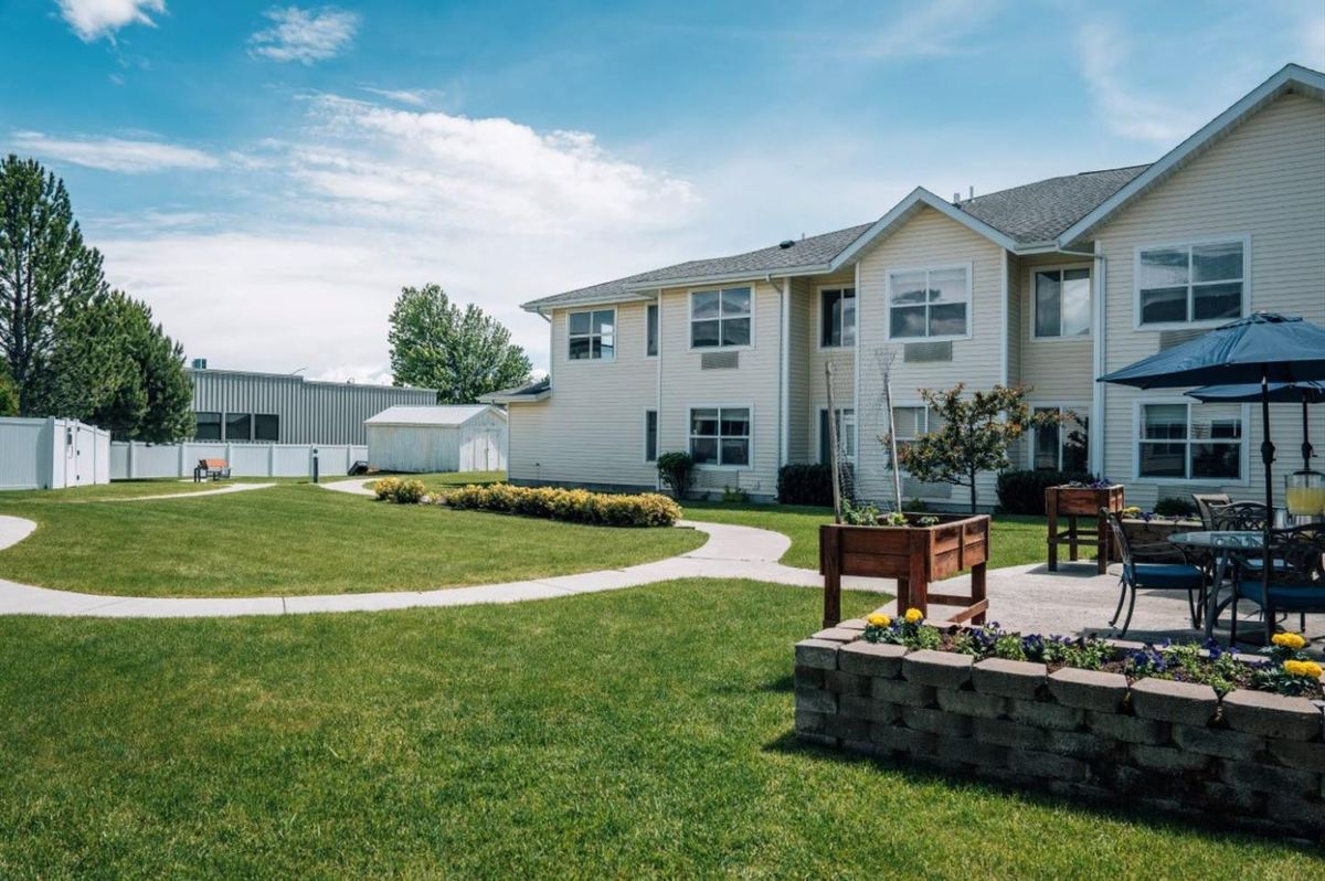 A well-maintained apartment complex with a lawn and benches under a partly cloudy sky.