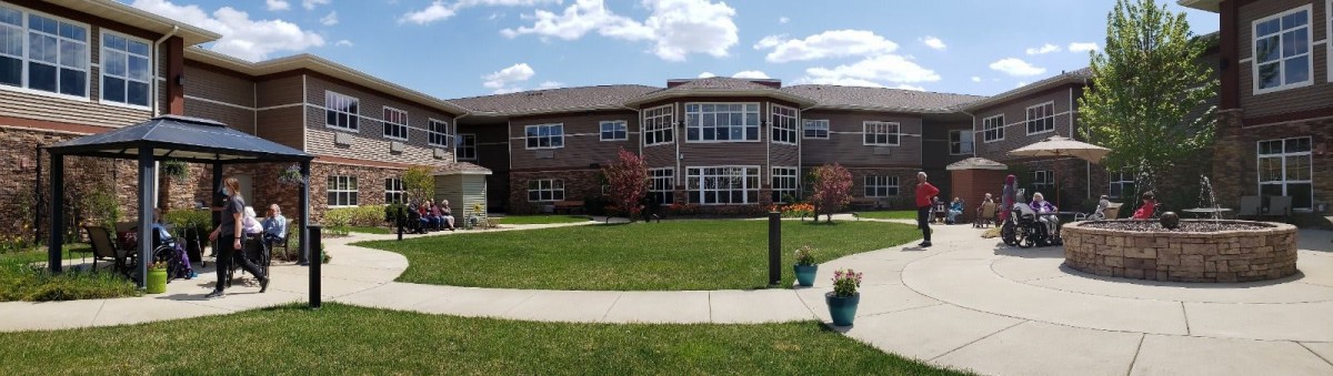 A two-story building with large windows, surrounded by a green lawn and pathways under a partly cloudy sky.