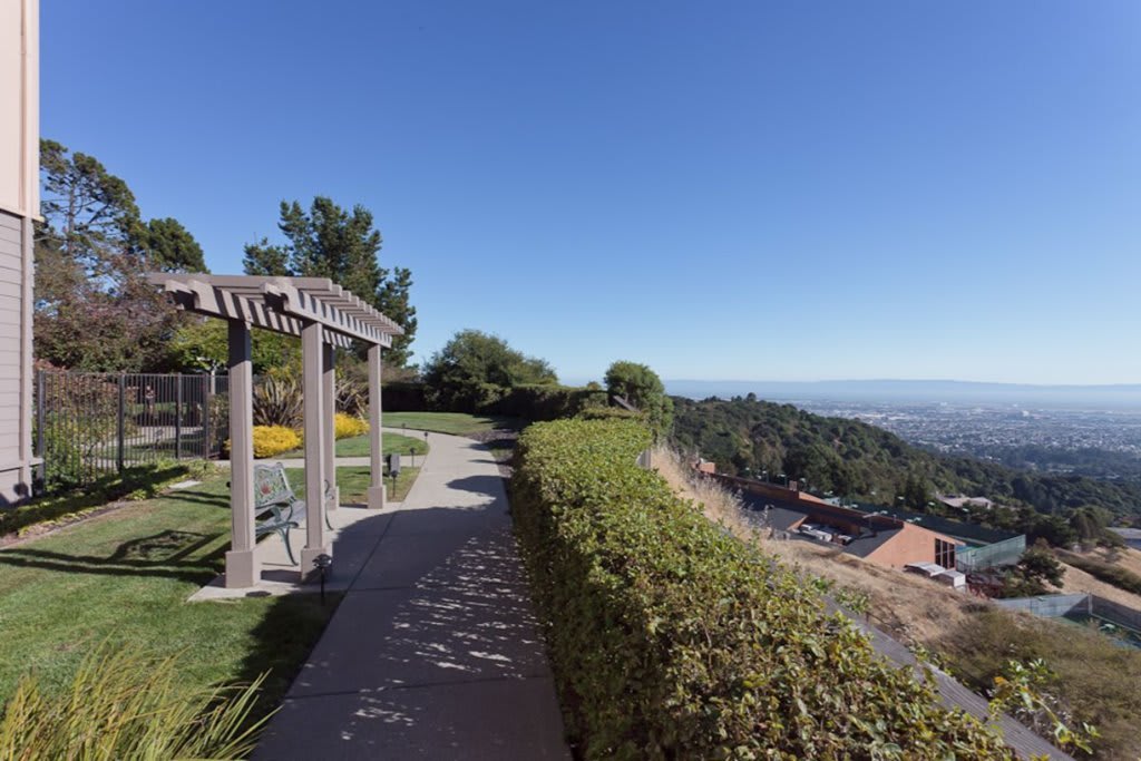 A scenic garden pathway with a pergola overlooking a vast landscape.