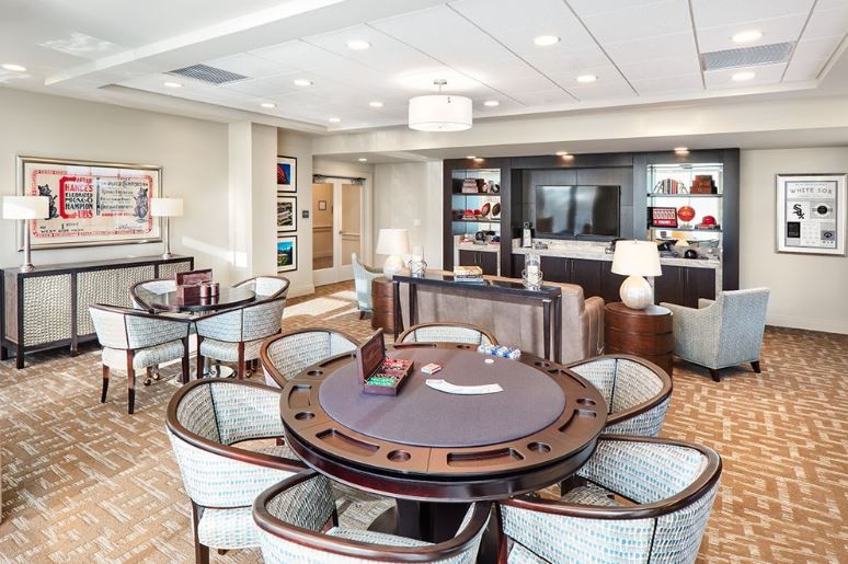 A modern lounge area with a poker table, surrounded by chairs and well-lit bookshelves.