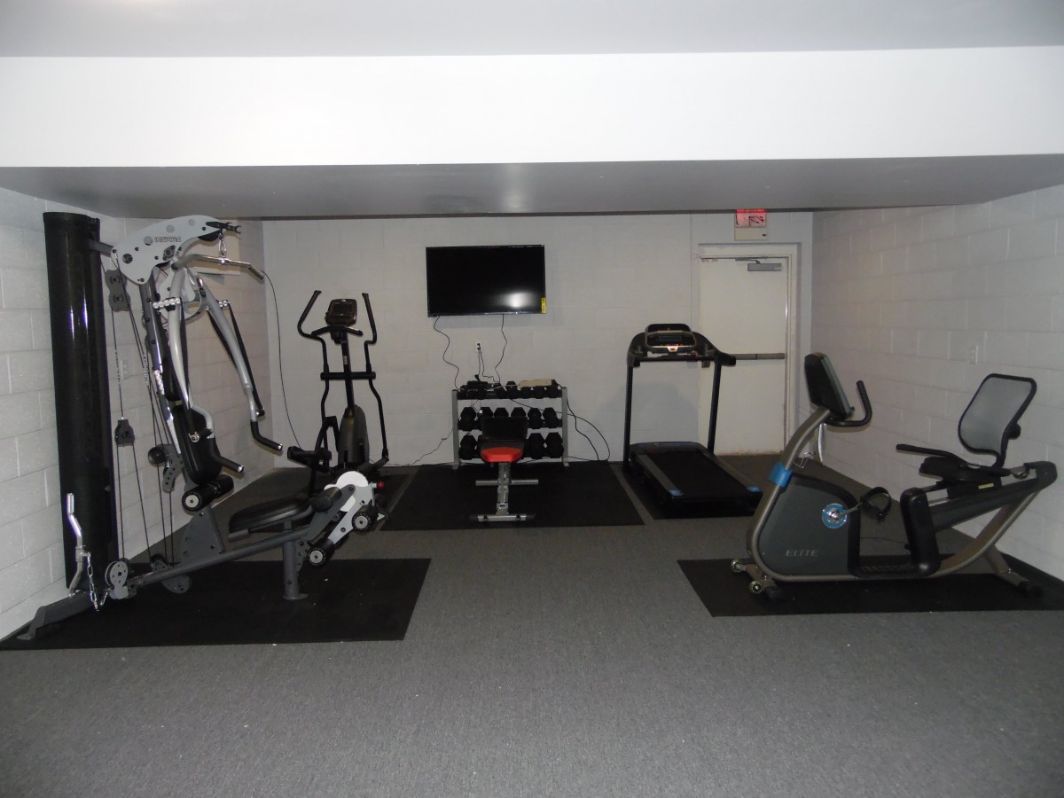 A gym room equipped with various exercise machines, including a treadmill, stationary bike, elliptical, and weights.