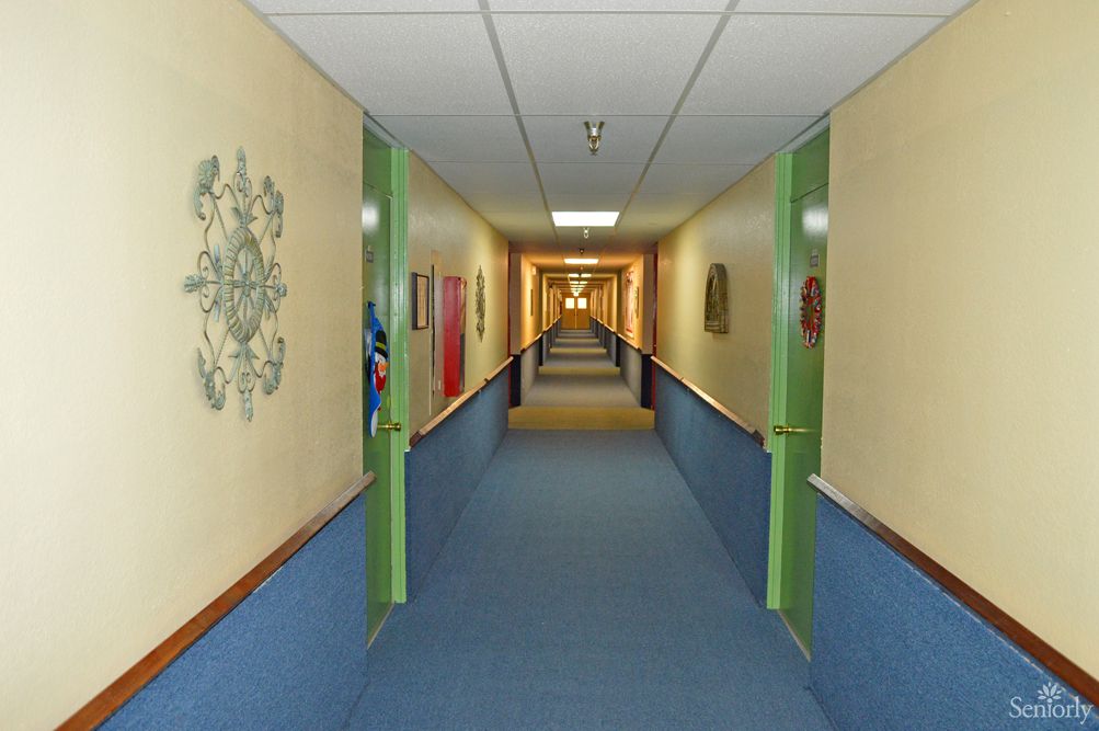 A long indoor corridor with green doors and blue carpeting.
