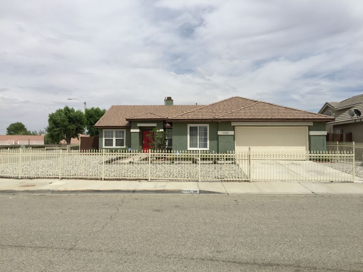 A single-story suburban house with a gated driveway under a cloudy sky.