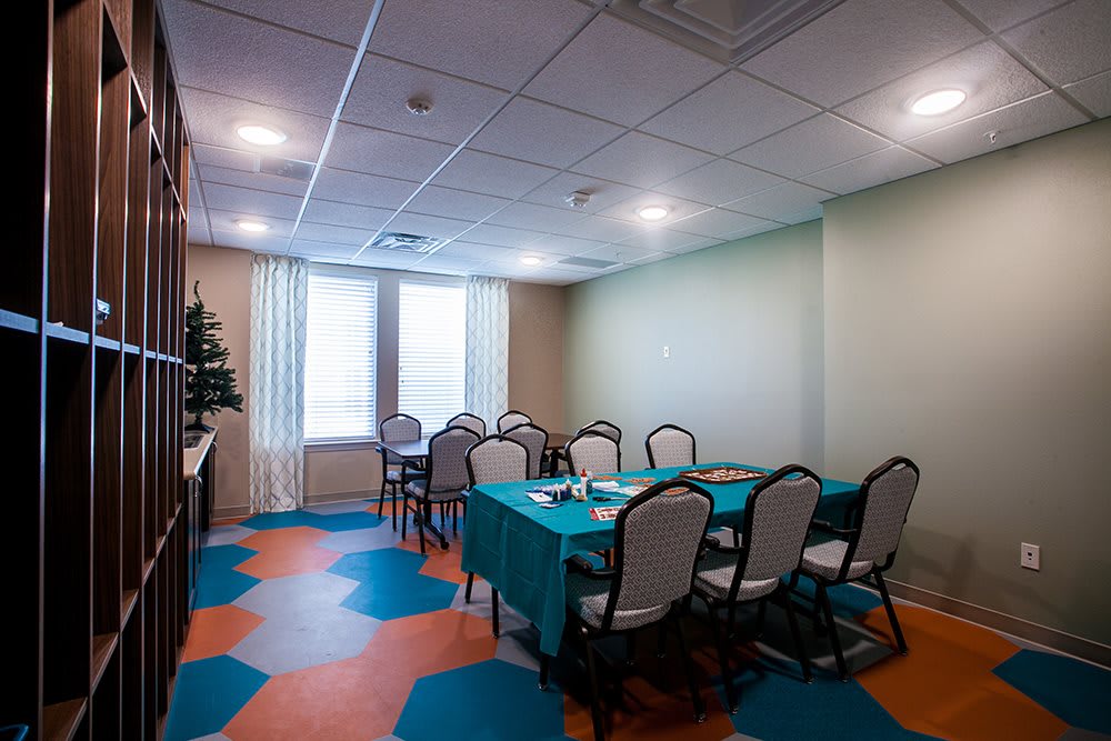 A small meeting room with a conference table and chairs, featuring colorful flooring and large windows.