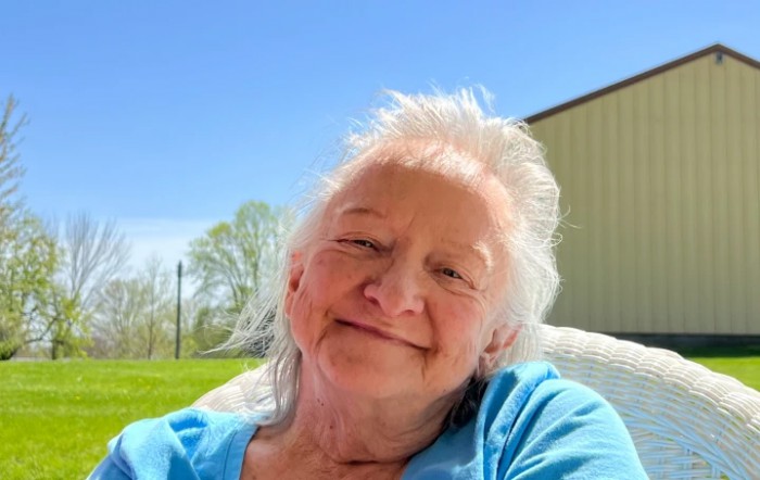 An elderly person smiling while sitting outside on a sunny day.