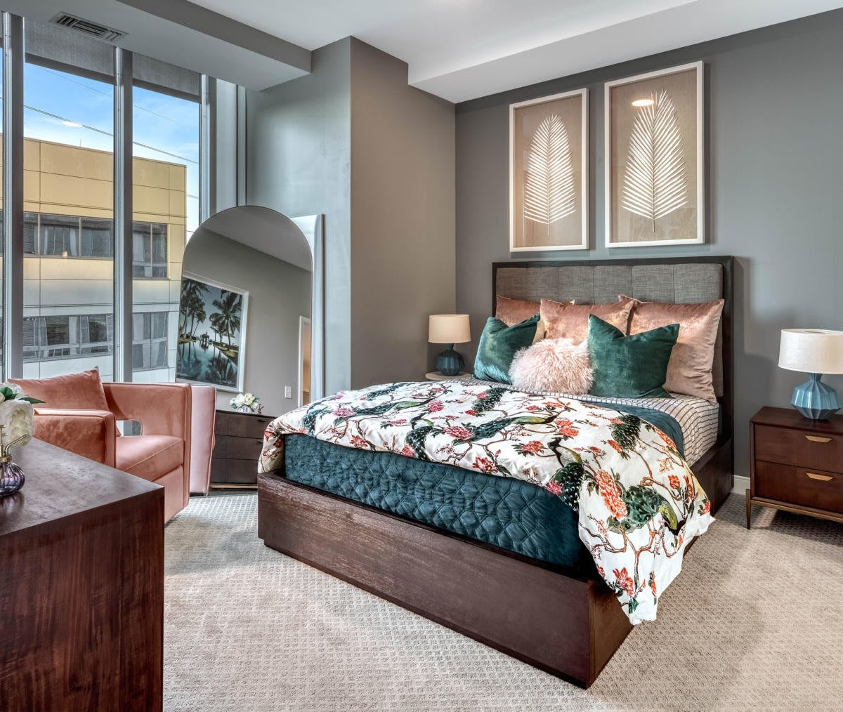 A modern bedroom with stylish decor, featuring a large bed, armchair, and artwork on the walls.