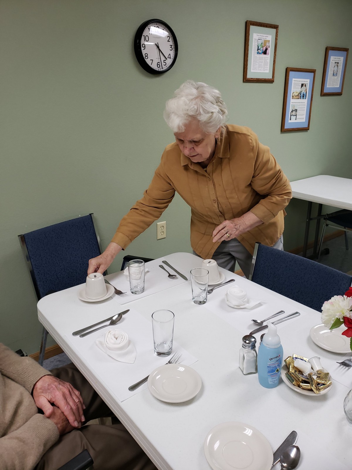 An elderly woman sets a dining table inside a restaurant.