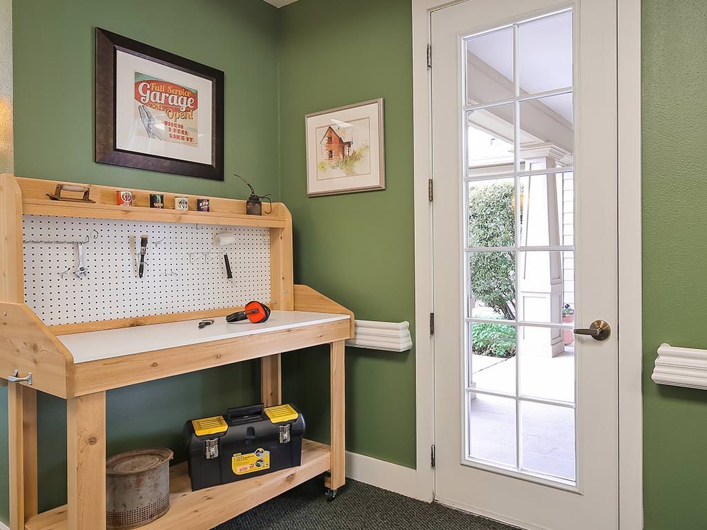 A tidy workshop area with a wooden workbench, pegboard for tools, and a toolbox against green walls next to a glass-paneled door.