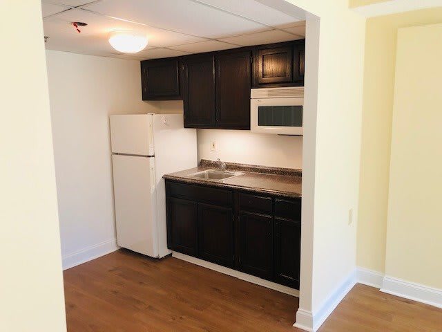 A compact kitchen setup with dark cabinets, a refrigerator, and a microwave.