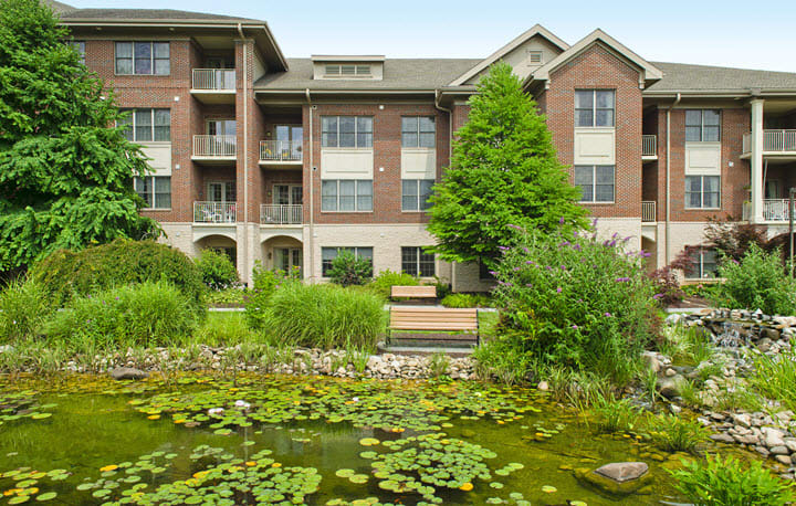 A scenic view of an apartment building with a garden and pond in the foreground.