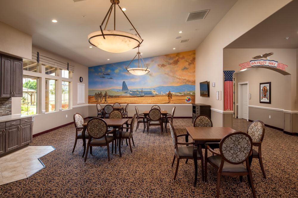 A dining area with tables and chairs, featuring a colorful mural on the wall and warm lighting fixtures.