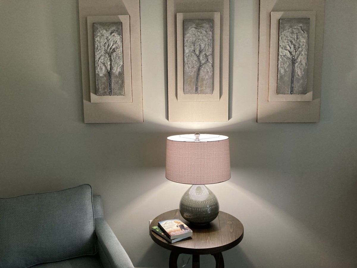 A cozy living room corner with a lit lamp, artwork on the wall, and a side table beside a sofa.
