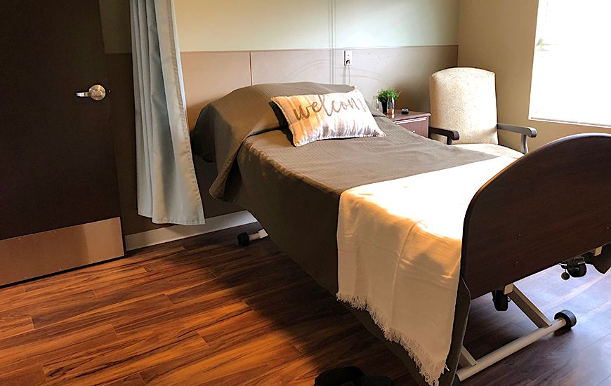 A cozy hospital room with a neatly made bed and comfortable seating.
