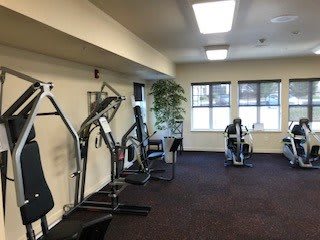 A well-lit gym room with exercise machines and fitness equipment.