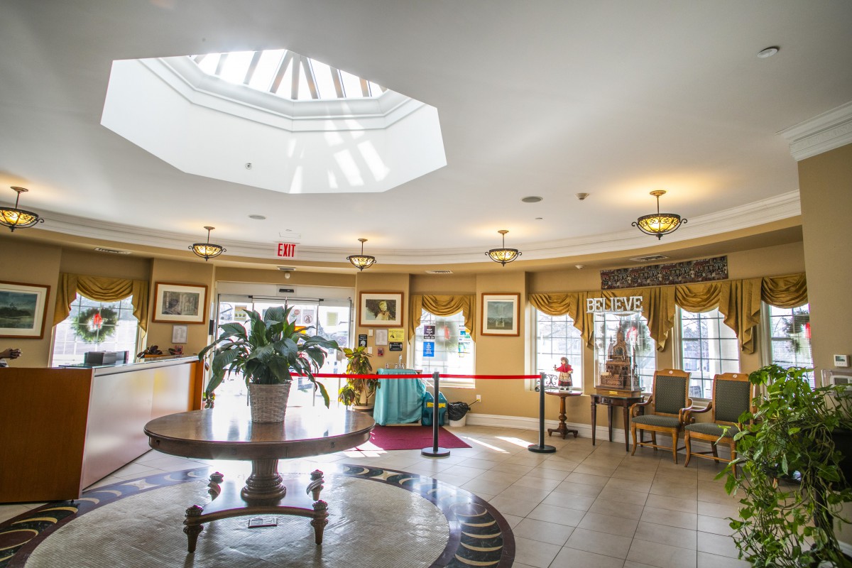 A well-lit lobby interior featuring elegant decor, a central table with a potted plant, and ample natural light from an overhead skylight.