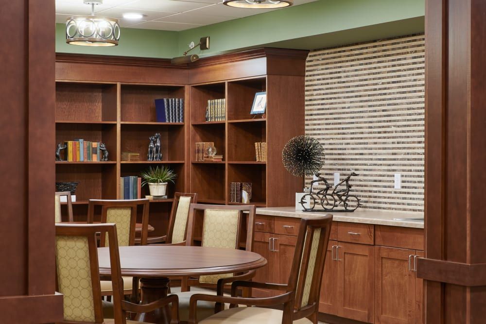 A cozy library room featuring wooden bookshelves, a round table, and chairs.