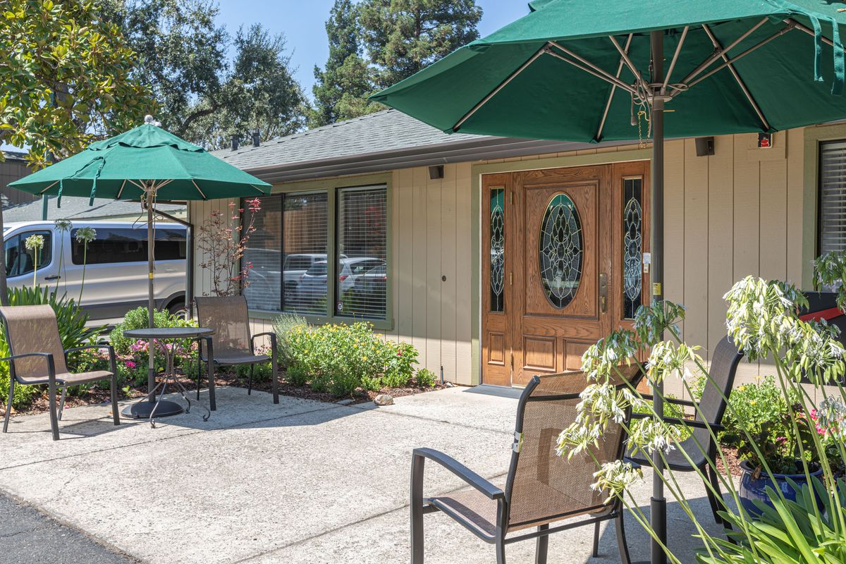 A cozy outdoor patio area with chairs, tables, and umbrellas in front of a building.
