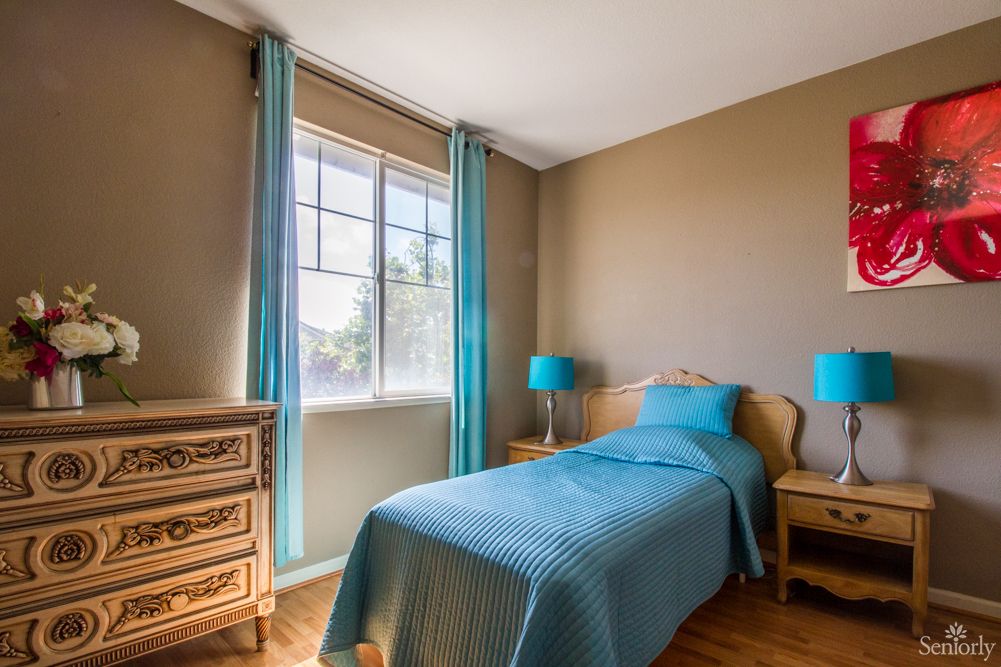 A cozy bedroom with a single bed and blue accents, illuminated by natural light.