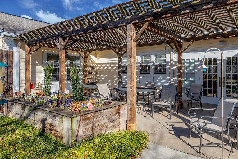 A sunny patio with a pergola, featuring outdoor seating and a raised garden planter.