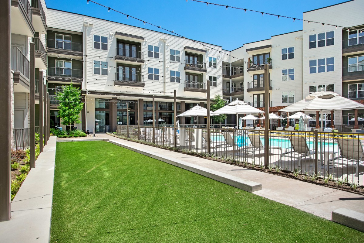 A modern apartment complex featuring a swimming pool and outdoor seating area, surrounded by well-maintained landscaping.