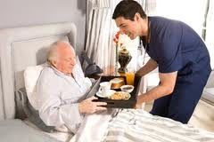A caregiver serves breakfast to an elderly man in bed.