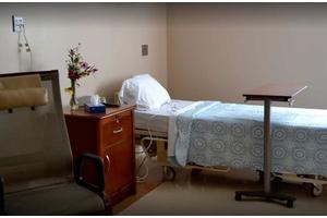 A hospital room with a single bed, bedside table, and floral arrangement.