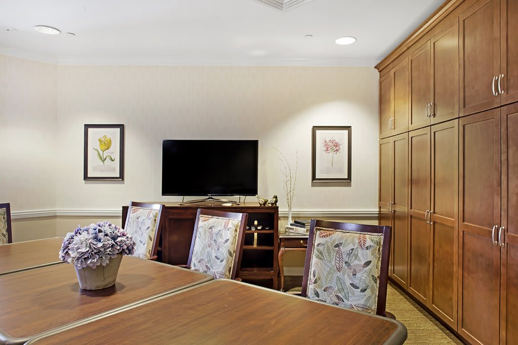 A cozy conference room with a large table, floral chair upholstery, wood paneling, and a television mounted on the wall.