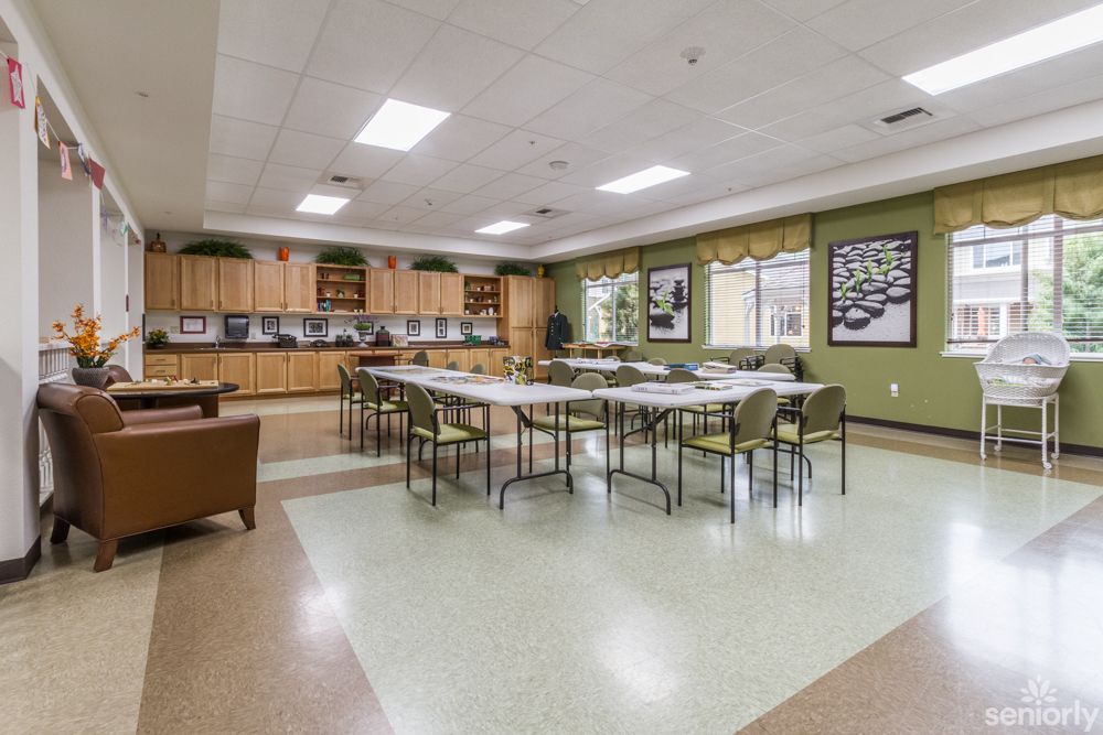 Spacious classroom with tables and chairs arranged in the center, surrounded by cabinets and windows.