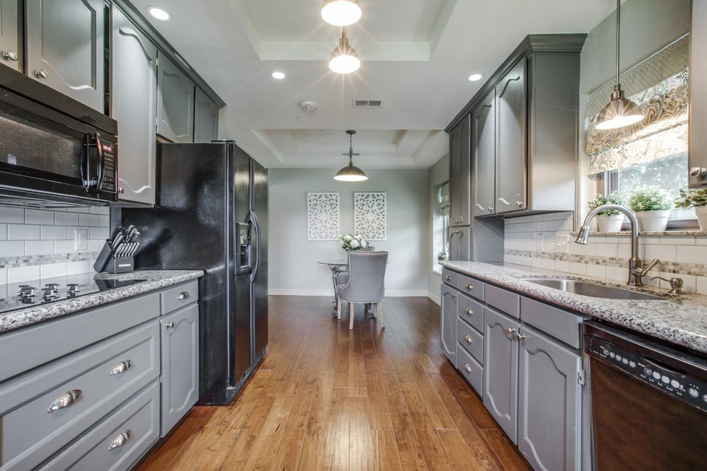 A modern kitchen with sleek cabinetry and hardwood flooring leading to a dining area.
