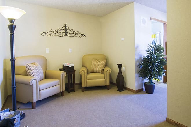 A cozy living room with two armchairs and decorative elements, including a wall piece and an indoor plant.
