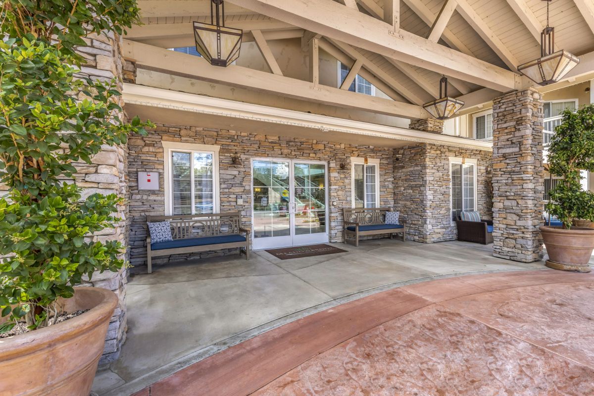A welcoming building entrance with stone walls and benches on a covered porch.