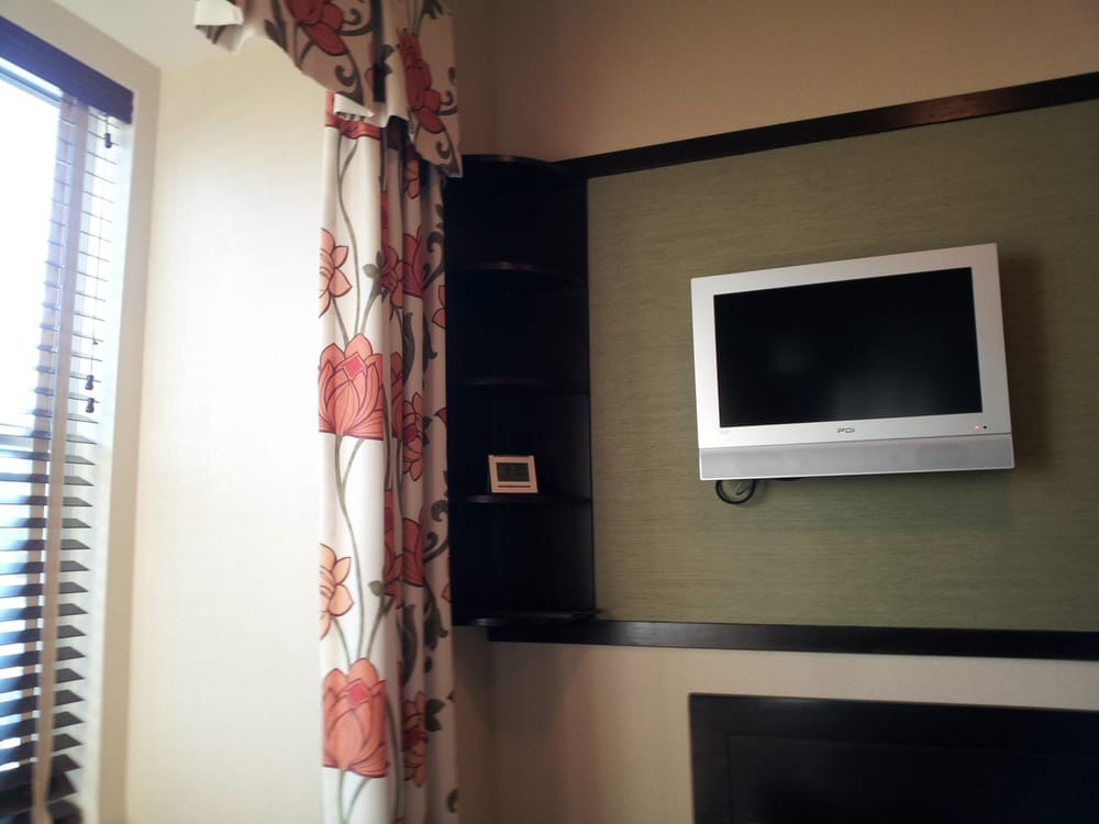 A wall-mounted television in a living room with floral curtains.