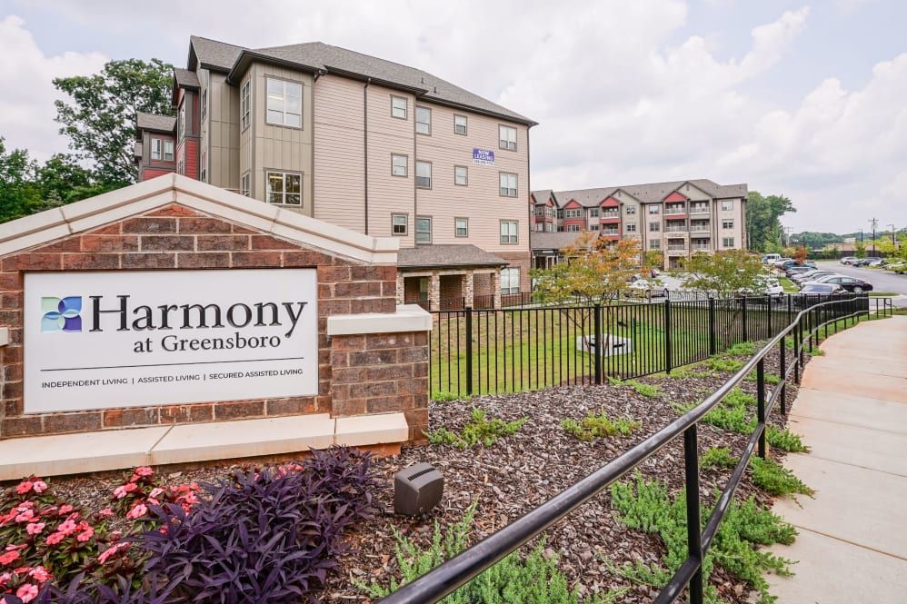 An exterior view of a residential apartment complex with a landscaped garden and signage in the foreground.