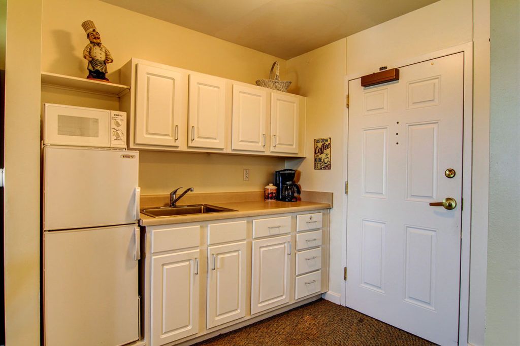 A small kitchen area with white cabinets, a refrigerator, microwave, and sink.