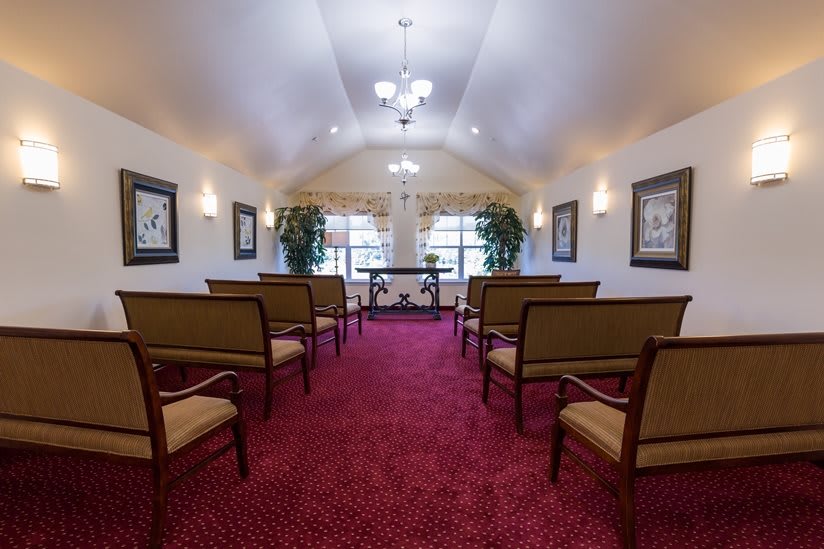 A small chapel interior with rows of seats, red carpet, and decorative elements.