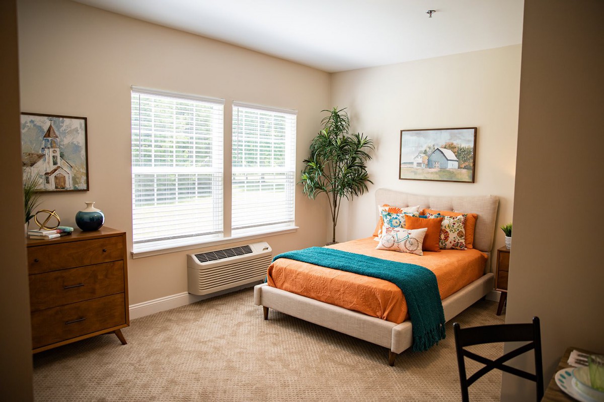 A cozy bedroom with a neatly made bed and warm lighting, featuring tasteful decor and natural light from the windows.