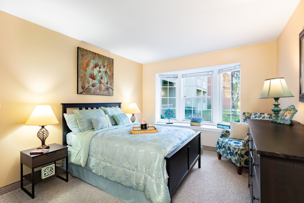 A cozy bedroom with a large window, featuring a neatly made bed and stylish decor.