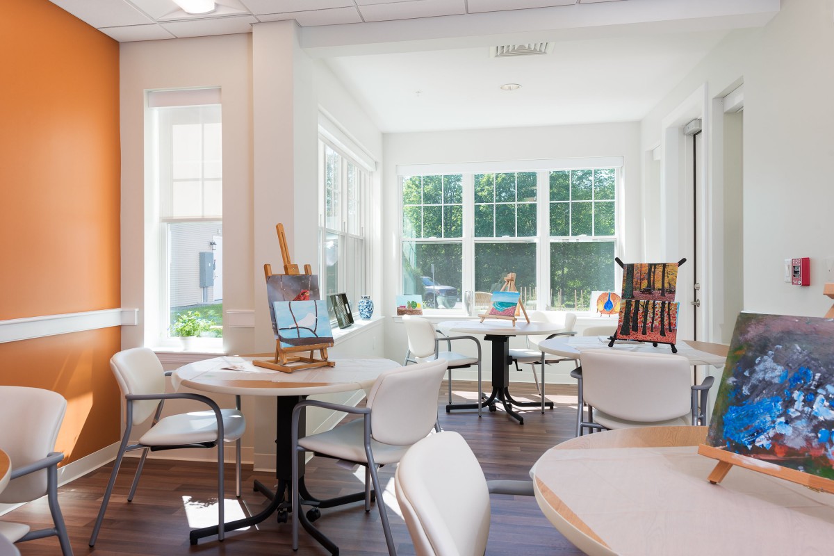 A bright and inviting art room filled with natural sunlight, featuring easels, tables, chairs, and art supplies.